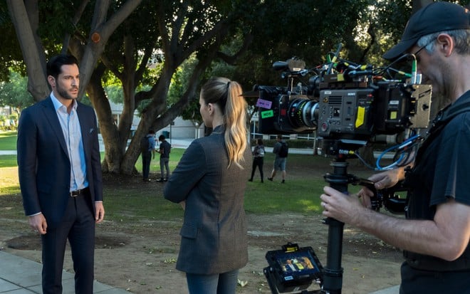 Homem segura uma câmera enquanto foca em Tom Ellis e Lauren German, que estão conversando