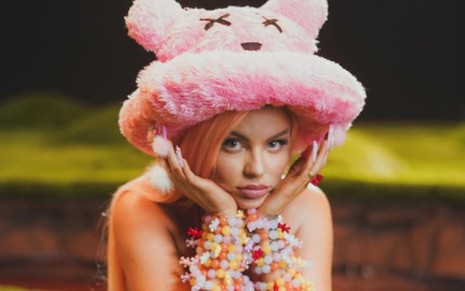 Luísa Sonza com chapéu rosa de ursinho e as mãos apoiadas no rosto no clipe da música Atenção