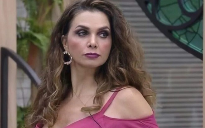 Luiza Ambiel em A Fazenda 12, com blusa amarela, sombra escura nos olhos, batom roxo, olha para a direita