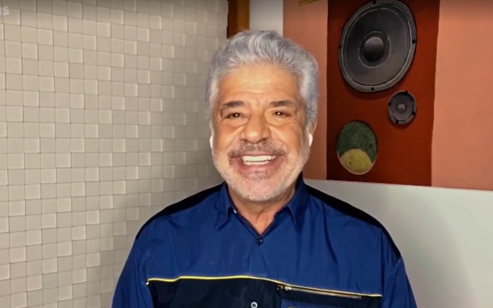 Lulu Santos sorridente em vídeo do Altas Horas, usando camisa azul com detalhes em preto