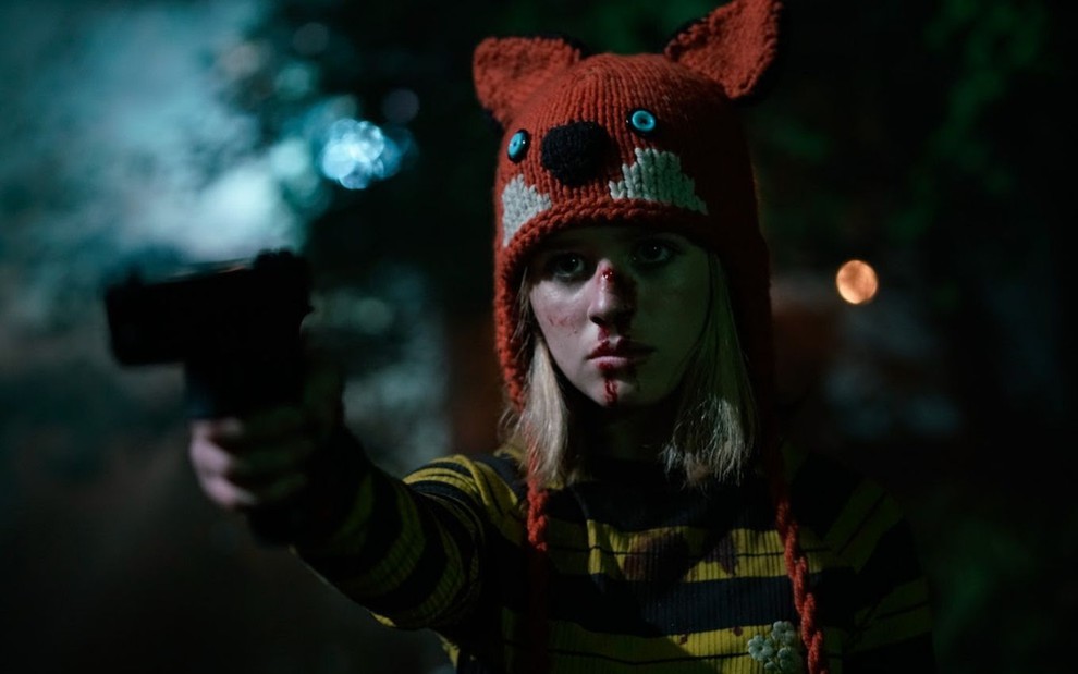 A atriz Lulu Wilson usa uma touca de raposa, está com o nariz sangrando e aponta uma arma para frente no filme Becky (2020)