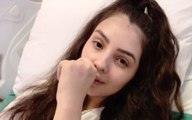 Mabel Calzolari deitada na cama de hospital, com a mão na boca