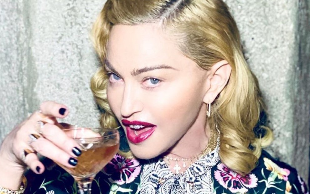 Madonna com uma taça na mão, de boca aberta e sorrindo 
