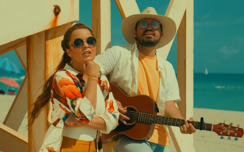 Maiara e Fernando na praia usando roupas coloridas e óculos escuros