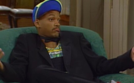 Sentado em uma poltrona, Will Smith faz gesto de indiferença em cena do primeiro episódio da comédia Um Maluco no Pedaço
