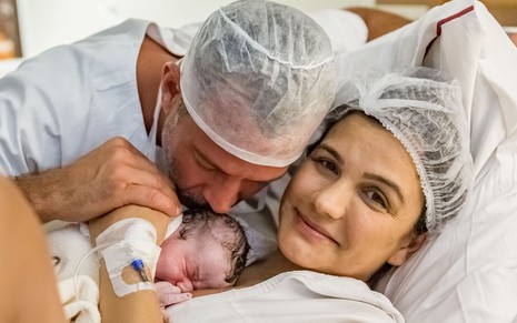 Malvino aparece com touca na cabeça, avental branco e beija o filho recém-nascido; Kyra posa para a foto e sorri