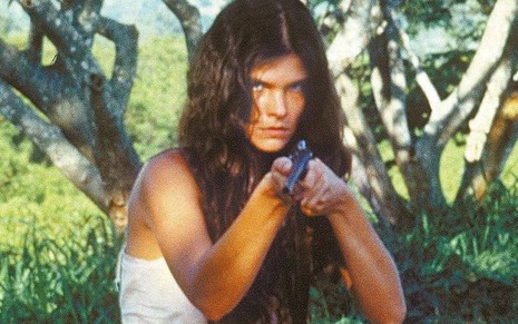 A atriz Cristiana Oliveira como a personagem Juma Marruá segurando uma espingarda na mão em cena de Pantanal, da Manchete, novela de 1990