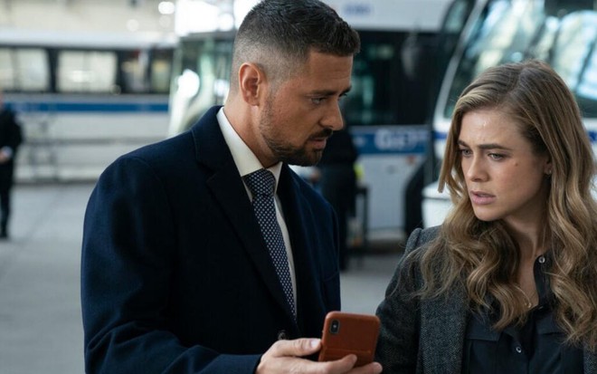 Dentro de uma garagem de ônibus, J.R. Ramirez mostra a tela de um celular para Melissa Roxburgh, em Manifest