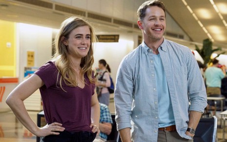 Protagonistas da série Manifest, Melissa Roxburgh e Josh Dallas sorriem dentro de um aeroporto