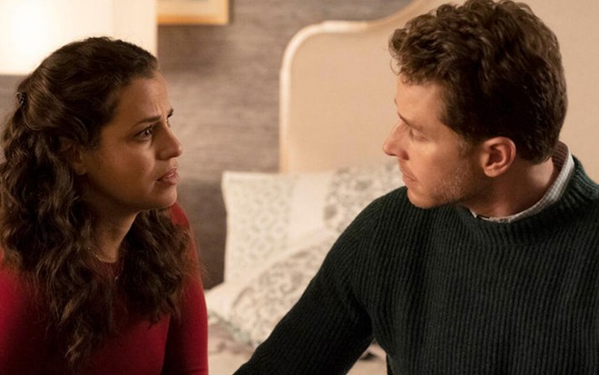 Dentro de um quarto, Athena Karkanis e Josh Dallas aparecem sentados na beira de uma cama de casal na série Manifest