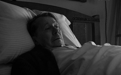 Gary Oldman deitado em uma cama com a cabeça em um travesseiro em cena de Mank (2020)