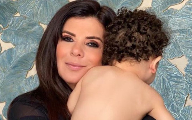 Mara Maravilha segura no colo o filho, Benjamin, que está de costas e sem mostrar o rosto