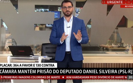 Marcelo Come no GloboNews Em Pauta, de terno azul, em pé e de óculos