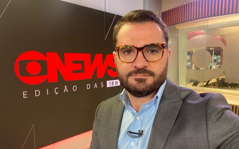 Marcelo Cosme ao lado de telão com a inscrição: GloboNews - Edição das 18h