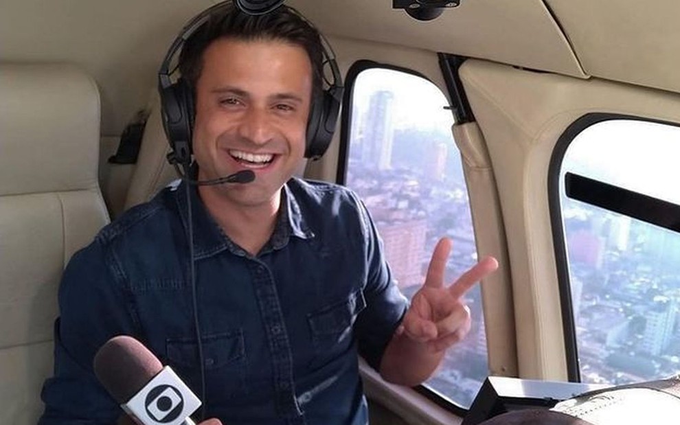 Marcelo Poli sorridente com o microfone da Globo na mão dentro da cabine do Gobocop