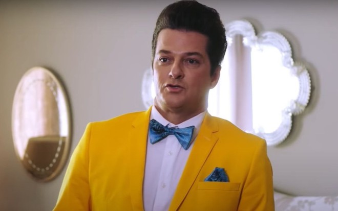 De terno amarelo e gravata azul, Marcelo Serrado faz biquinho na pele de Crô