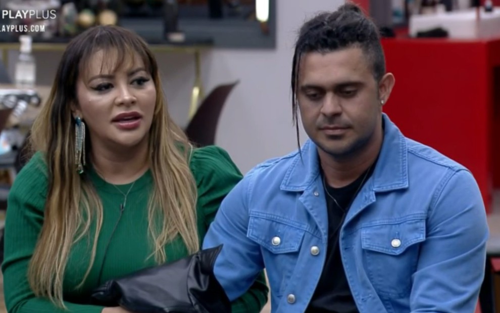Márcia Fellipe com uma blusa verde, e Rod Bala com uma camisa jeans, sentados em um banco na D.R. do Power Couple Brasil