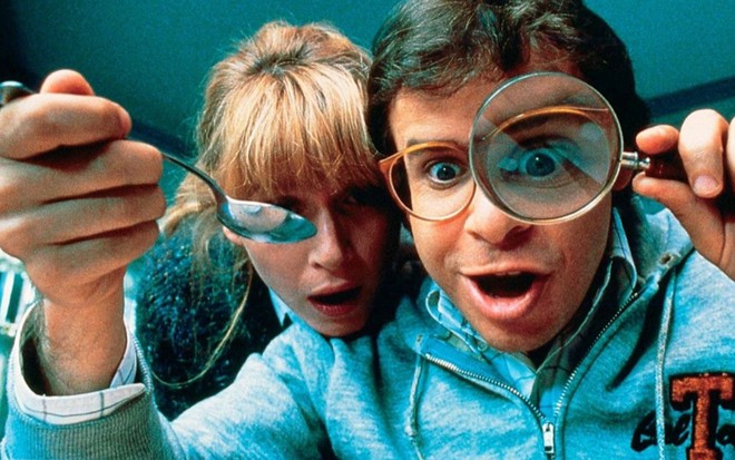 Marcia Strassman está encostada no ombro de Rick Moranis; o homem segura uma colher e uma lupa em cena de Querida, Encolhi as Crianças (1989)