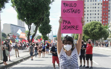 Imagem de Maria Ribeiro segurando cartaz em homenagem a Paulo Gustavo durante protesto