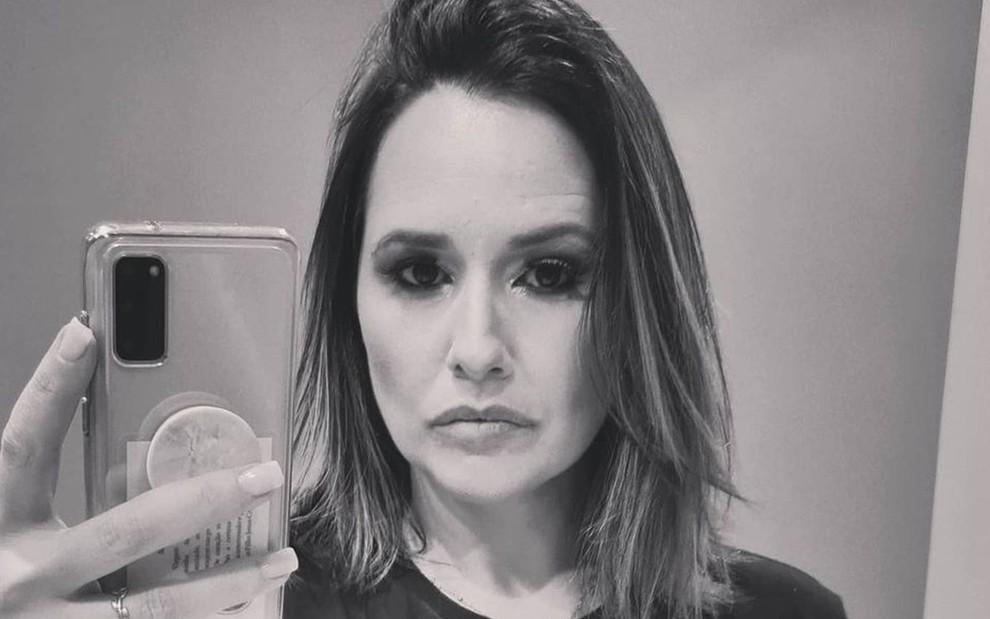 Mariana Belém em foto preto e branco, segurando o celular, com uma camiseta escrita "abuso"