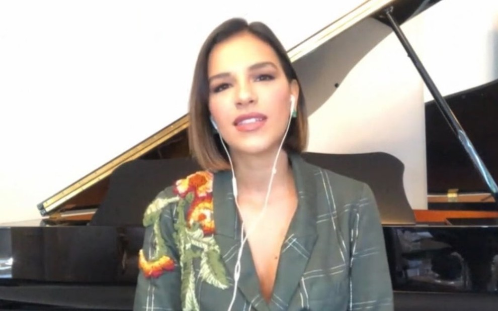 Mariana Rios, de blusa verde, está sentada em frente a um piano, durante entrevista por videochamada no Encontro