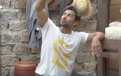Mariano com uma camiseta branca de estampa amarela, apoiado com um braço e levantando o outro