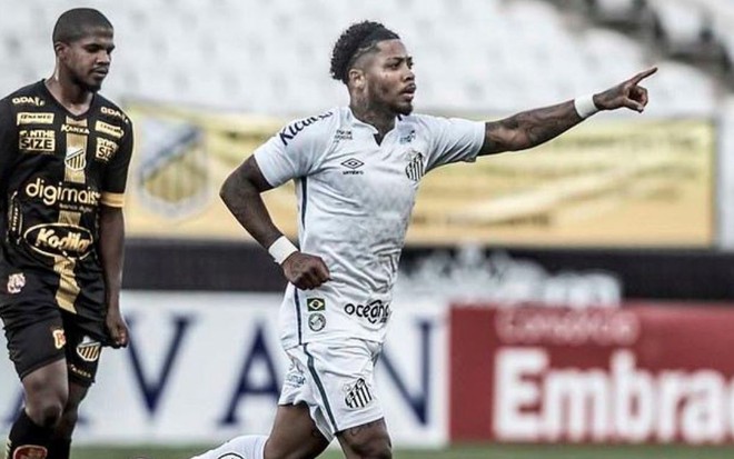 Imagem mostra um jogador do Santos comemorando um gol e outra atleta do Novorizontino ao fundo