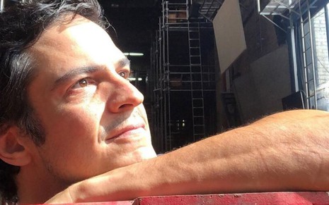 O ator Mateus Solano apoiado em uma estrutura vermelha olhando para cima em imagem publicada em rede social