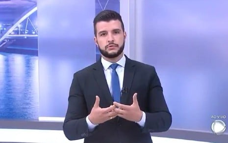 De terno preto, camisa branca e gravata azul, o apresentador Matheus Ribeiro gesticula durante seu comentário no DF Record