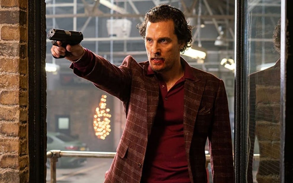 Matthew McConaughey aponta uma arma para frente em cena do filme Magnatas do Crime (2020)