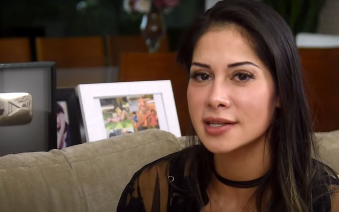 Mayra Cardi sentada em um sofá, com a boca semiaberta, concedendo entrevista