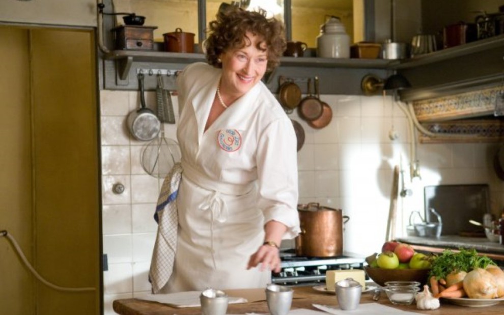 Meryl Streep com vestes de chef, em uma cozinha, sorrindo
