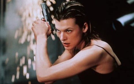 Milla Jovovich como Alice Resident Evil: O Hóspede Maldito, agachada ela segura uma arma em mãos em posição espreita