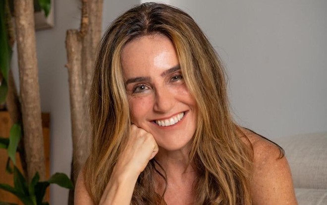 A atriz Monique Curi, com a mão apoiada no rosto, sorrindo para foto