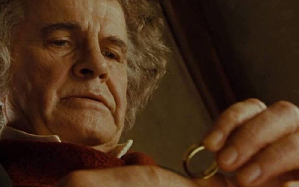 Imagem de Ian Holm caracterizado como Bilbo, olhando para um anel 