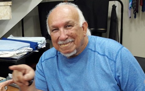 Imagem de João Bosco Tureta sorrindo, em casa, usando uma camiseta azul