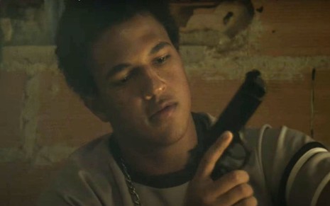 O ator Jorge Dias observa uma arma de fogo em cena do filme Na Quebrada (2014)
