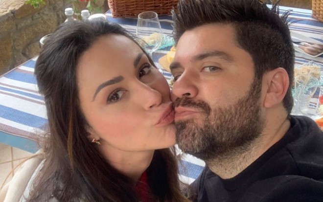 Nadja Haddad e o marido Danilo Joan dando um selinho enquanto olham para a câmera