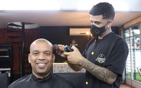 Luiz Alano sorrindo ao lado do filho na barbearia deles, ambos de preto