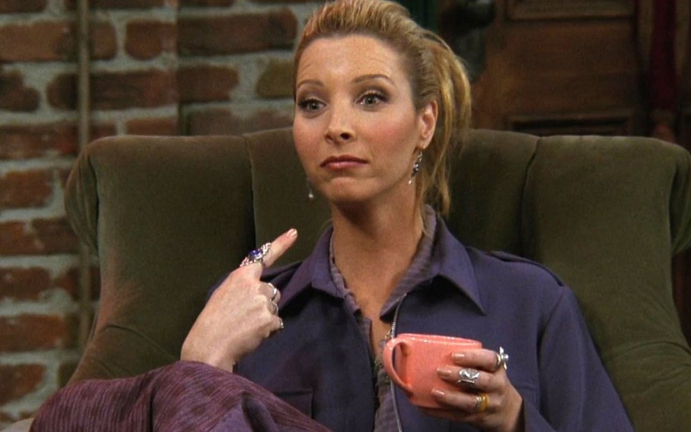 Lisa Kudrow como Phoebe Buffay no sofá do Central Perk da série Friends