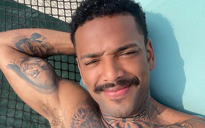 Nego do Borel sem camisa, de bigode, tomando sol