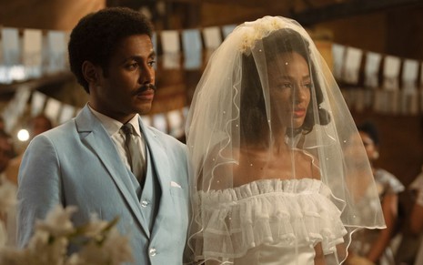 Ícaro Silva, de terno azul, está ao lado de Pathy Dejesus, com um vestido de noiva branco e véu no rosto, em cena de Coisa Mais Linda