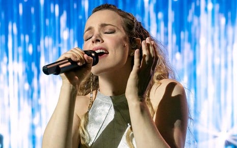 A atriz Rachel McAdams em cena do filme Festival Eurovision da Canção: personagem usa vestido branco e canta com olhos fechados