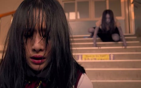 A atriz SeolA está com os cabelos na frente do rosto em uma escada enquanto é perseguida por um fantasma acizentado em cena de Goedam