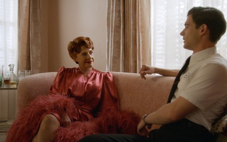 Avis Amberg (Patti LuPone), sentada no sofá com apenas um robe de seda, olha de maneira sedutora para o aprendiz de galã Jack Castello (David Corenswet)