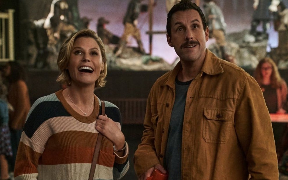 No que aparenta ser um festival, Julie Bowen e Adam Sandler estão observando algo com expressão feliz em O Halloween do Hubie (2020)