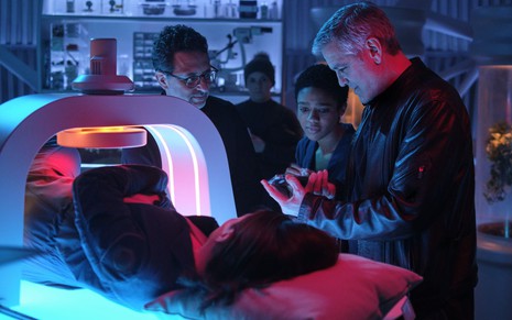 Felicity Jones está deitada em uma máquina moderna, sendo observada pelo produtor Grant Heslov, pela atriz Tiffany Boone e pelo ator e diretor George Clooney