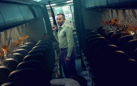 Armado, o personagem Terenzio (Stefano Cassetti) segura uma arma dentro de um avião escuro