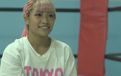 Com cabelo rosa e camiseta branca, Hana Kimura esboça sorriso no ringue em cena do reality Terrace House