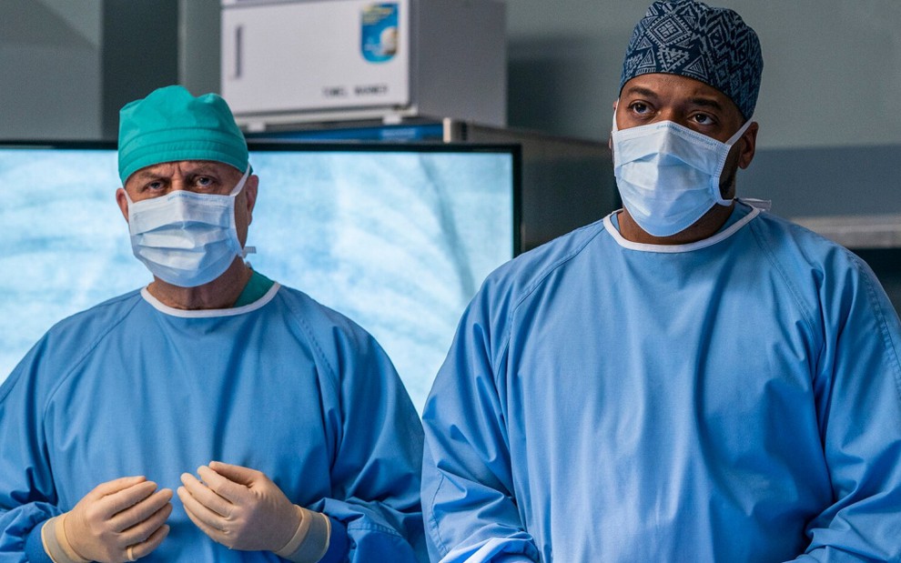 Com máscaras cirúrgicas no rosto e vestindo roupas de médico, Anupam Kher e Jocko Sims atuam em New Amsterdam